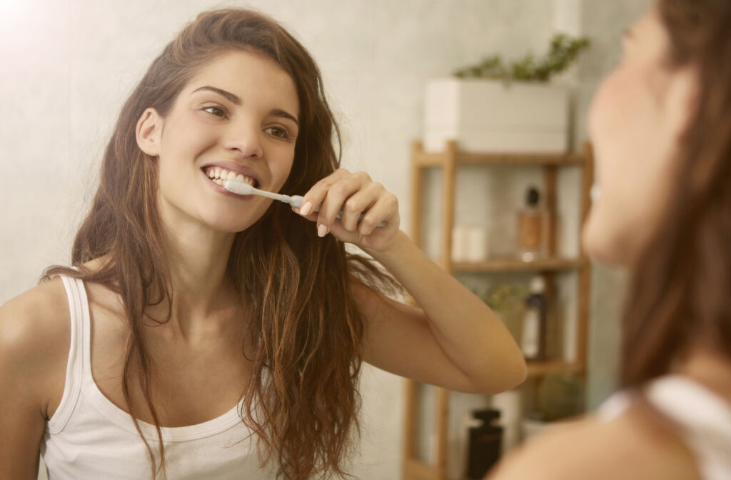 A young woman standing in front of a mirror brushing her teeth with a toothbrush.